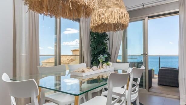 A dining area with a glass table and white chairs, overlooking a beach and the sea. - MAR COLONIA - Apartment with sea views in Colonia de Sant Jordi. Free WiFi (Ses Salines)