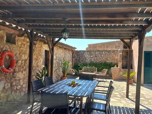 Une terrasse extérieure avec une table et des chaises, une bouée de sauvetage et un mur en pierre.