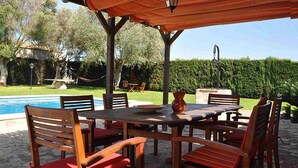 Une terrasse extérieure avec une piscine, des meubles en bois et une pergola agrémentée d’une lanterne.