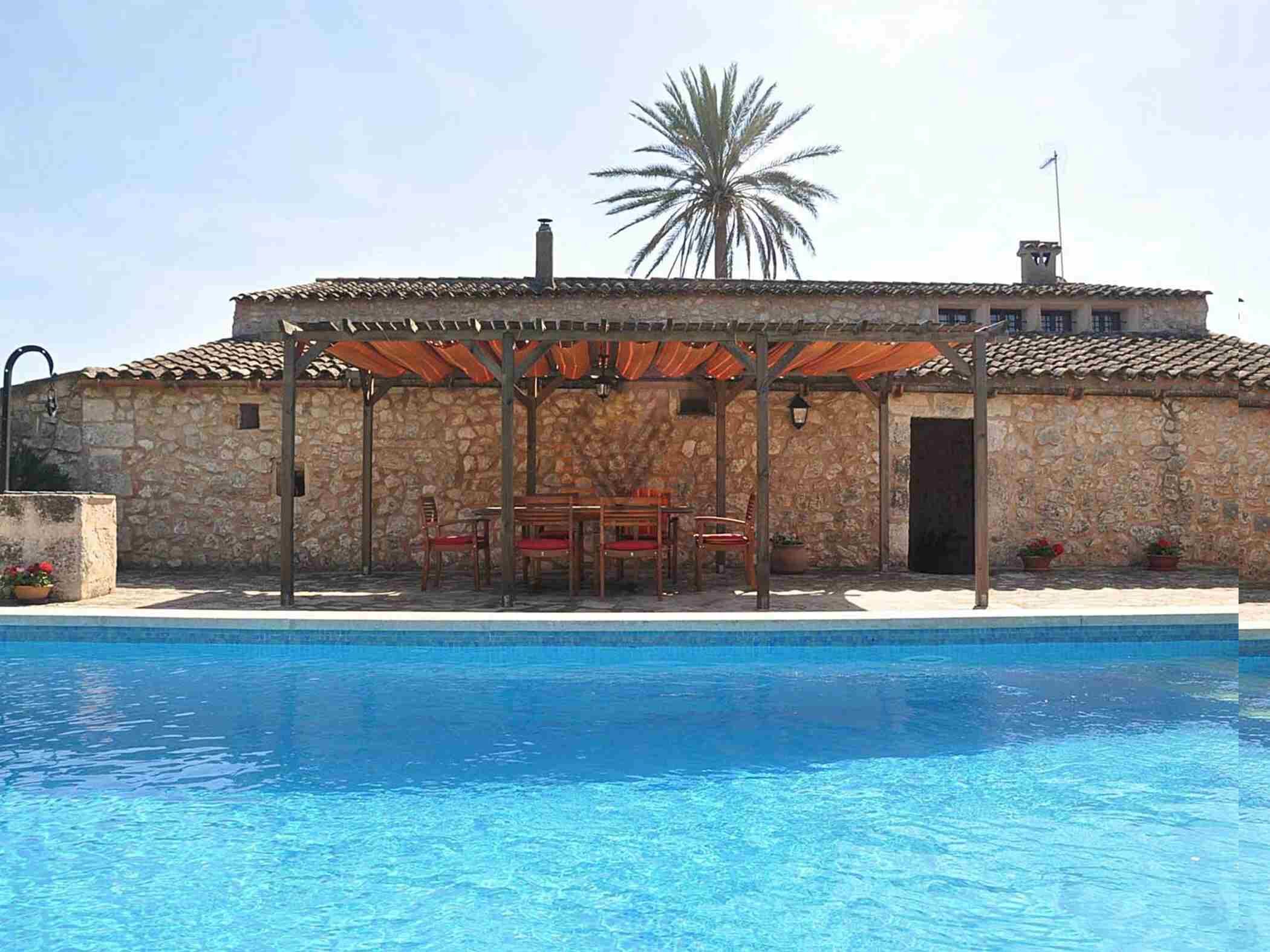 A stone building with a pool, outdoor seating, and a palm tree.