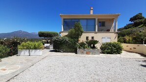 A two-story building with a balcony, surrounded by well-maintained gardens and a clear view of a mountain in the background. - Casa Régina - T3 N ° 1 / Ground garden SPACIOUS -  sumptuous sea view (Propriano)
