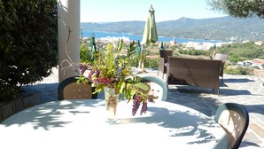 A round table with a vase of flowers, a wicker chair, and an umbrella. - Casa Régina - T3 N ° 1 / Ground garden SPACIOUS -  sumptuous sea view (Propriano)