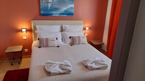A neatly made bed with white bedding and multiple pillows, two bedside tables, a small wooden stool, and a painting on the wall. - Casa Régina - T3 N ° 1 / Ground garden SPACIOUS -  sumptuous sea view (Propriano)