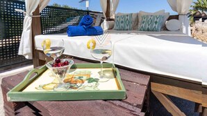 A bed with a white bedspread, a blue towel, and patterned pillows. A tray with a glass of wine and a fruit bowl is in front of the bed. - Torre Dorada, just 150 metres from Es Morer Vermell beach in Alcudia (Alcudia)