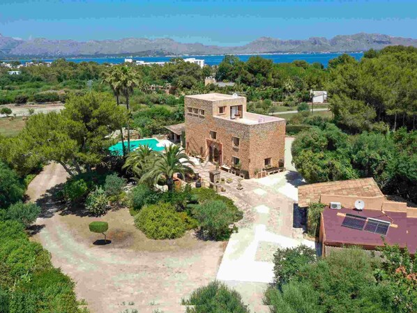 A stone building with a pool, surrounded by lush greenery and a view of the sea. - Torre Dorada, just 150 metres from Es Morer Vermell beach in Alcudia (Alcudia)