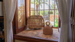 A room with a wicker chair, a clay pot, and a view of palm trees through a window with curtains. - Torre Dorada, just 150 metres from Es Morer Vermell beach in Alcudia (Alcudia)