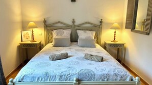 A double bed with a patterned bedspread, two bedside tables with lamps, a wall-mounted light fixture, and a mirror with shutters. - Mas de Pont Royal - Golf Estate - Pool & Garden (Mallemort)