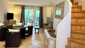 A living room with a sofa, a dining table, and a TV. There is a staircase with a decorative mirror. - Mas de Pont Royal - Golf Estate - Pool & Garden (Mallemort)