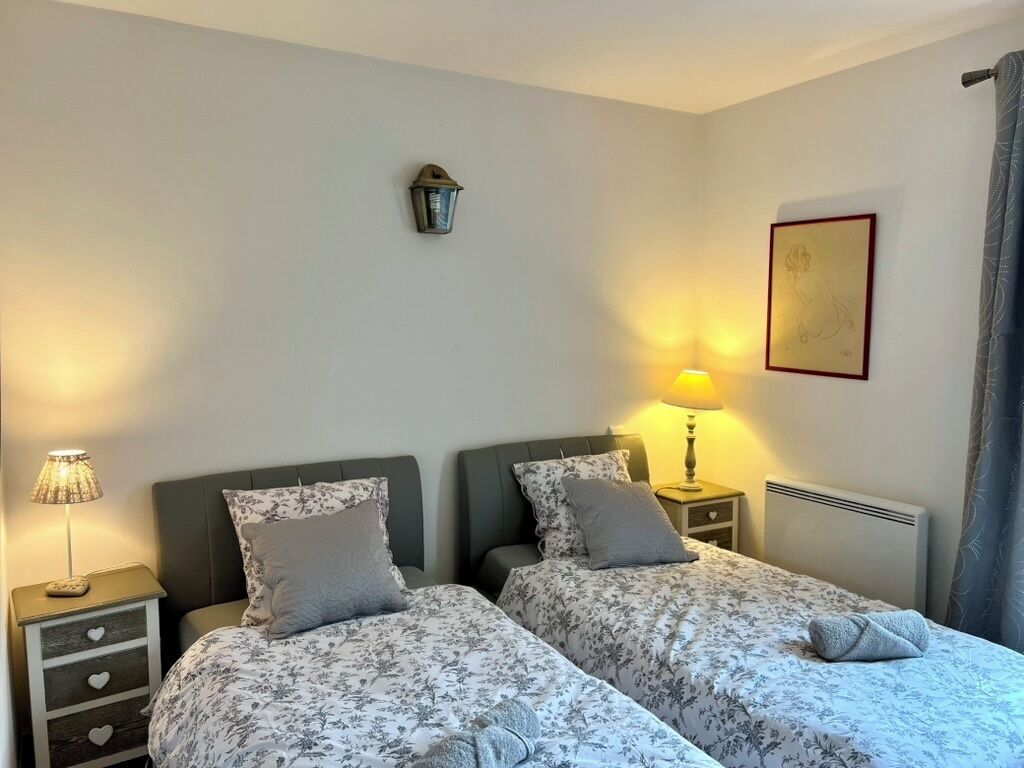 Une chambre avec deux lits, une table de chevet avec une lampe, une lampe fixée au mur et un tableau encadré.