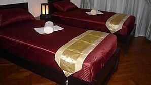 Ett hotellrum med två sängar, var och en med ett rött överkast och en guldfärgad detalj. Mellan sängarna står ett nattduksbord med en lampa.