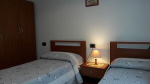 A bedroom with two beds, wooden headboards, a bedside table with a lamp, and a wardrobe. - Panoramic apartment with fantastic views of the sea (Buggerru)