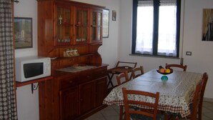 A dining area with a wooden cabinet, a microwave, a table with a floral tablecloth, and chairs. - Panoramic apartment with fantastic views of the sea (Buggerru)