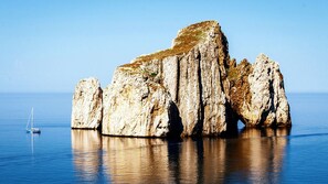 A large rock formation in calm water with a sailboat nearby. - Panoramic apartment with fantastic views of the sea (Buggerru)