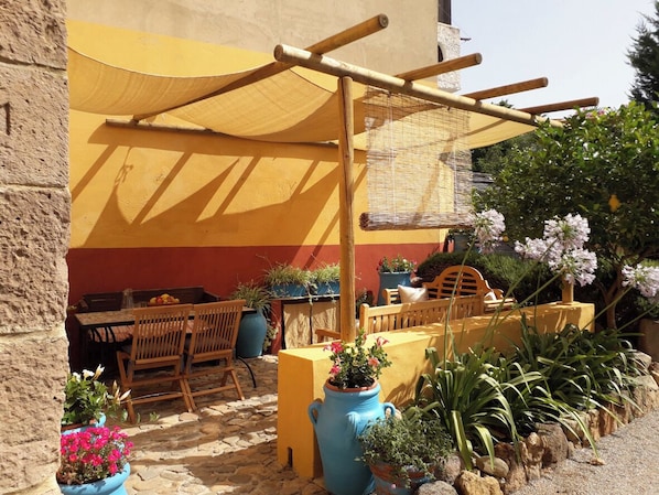 A patio with a table and chairs, a wooden bench, potted plants, and a pergola structure.