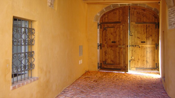 A corridor with a large wooden door, a window with metal bars, and a cobblestone floor. - The Ancient House, wonderful Sardinia! (Masainas)
