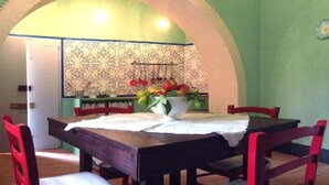 A dining area with a table set for four, surrounded by red chairs, and a decorative wall with hanging kitchen utensils. - The Ancient House, wonderful Sardinia! (Masainas)