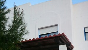 A white building with a red roof, a wooden fence, and a flowering plant in front. - House and garden, quiet area, near the beach (San Jose)