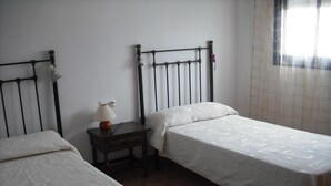 A bedroom with two single beds, a nightstand with a lamp, and a window with curtains. - House and garden, quiet area, near the beach (San Jose)