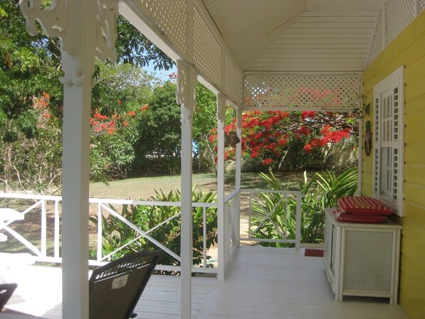 A covered porch with white railings, a bench, and a small table with a red cushion. - Gingerbread Cottage 2 bed with pool, seaviews, Nr Holetown St. James (Mount Standfast)