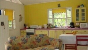 A compact living space with a sofa, a small table, a kitchen area with cabinets and a microwave, and a window with blinds.