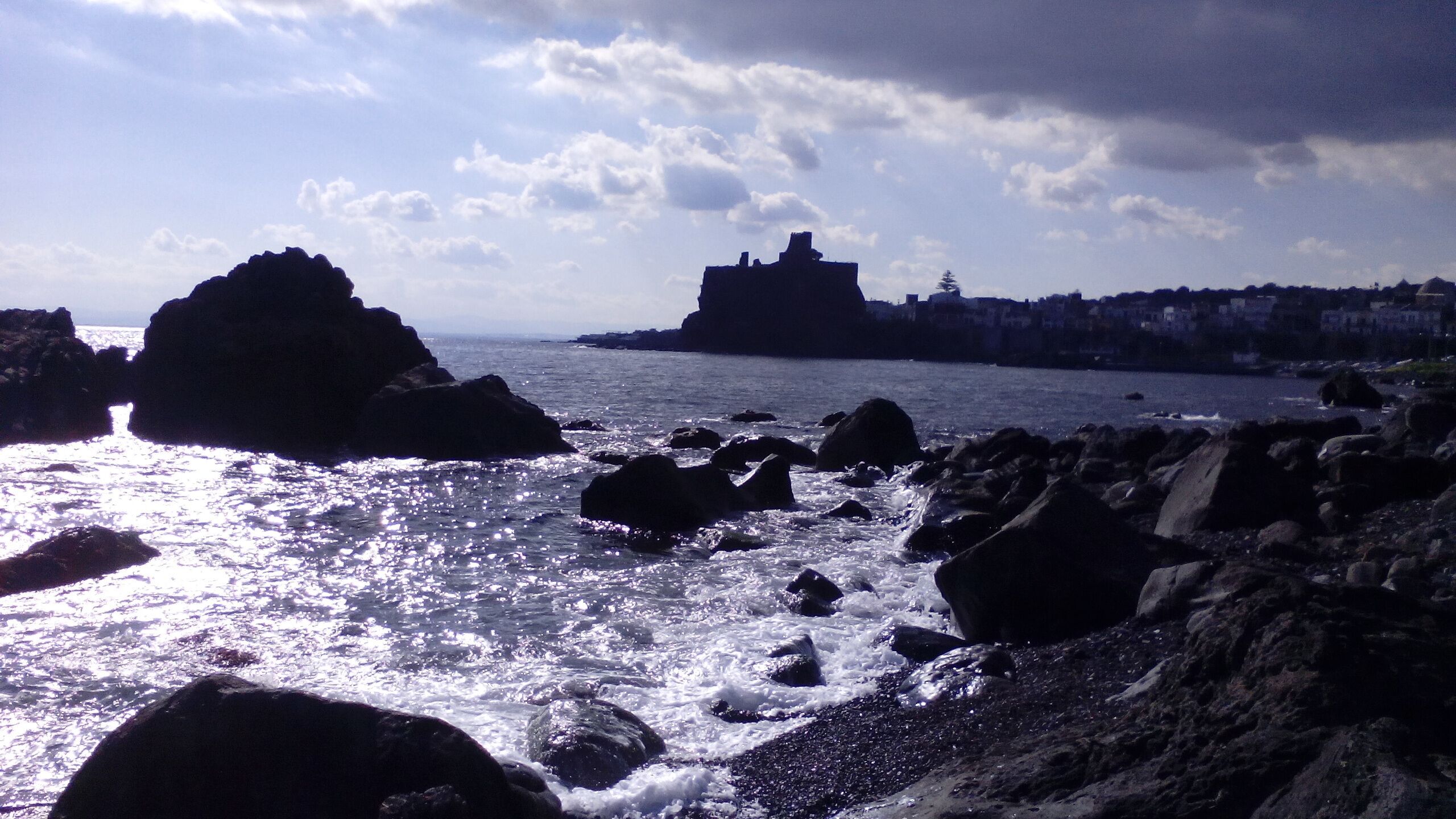 A coastal scene with rocky shores and a distant building on a cliff.