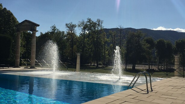Une piscine avec jets d’eau, une pergola et une vue sur les montagnes en toile de fond.