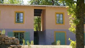 Un bâtiment à deux étages, avec un mur en pierre à l’avant, des volets verts et un escalier menant à l’étage supérieur.