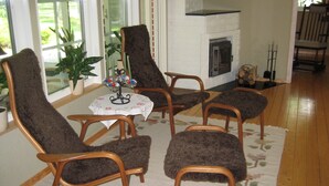 A cozy living room with a fireplace, wooden chairs, and a table with a floral tablecloth. - Lovely cottage in Juleboda a short walk from the fine sandy beach. (Degeberga)