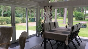 A covered patio with a dining table and chairs, large windows, and a view of a garden. - Lovely cottage in Juleboda a short walk from the fine sandy beach. (Degeberga)
