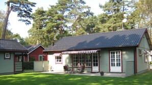 A two-story building with a covered patio area, surrounded by a well-maintained lawn and tall trees. - Lovely cottage in Juleboda a short walk from the fine sandy beach. (Degeberga)