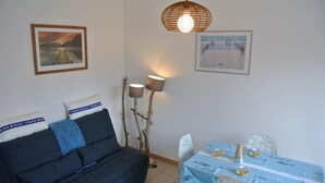 A room with a sofa, a dining table with chairs, two wall-mounted lamps, and two framed pictures.