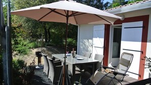 An outdoor patio with a table and chairs, a large umbrella, and a view of a garden and trees.