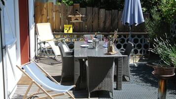 Een terras buiten met rieten meubels, een eettafel en een lounge stoel.