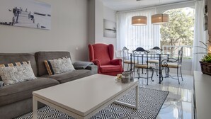 Ein modernes Wohnzimmer mit einem grauen Sofa, einem roten Sessel, einem weißen Couchtisch und einem Essbereich mit einem Metalltisch und Stühlen.