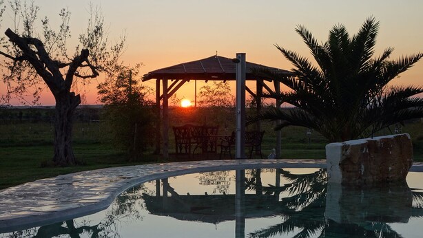 A serene outdoor setting with a reflective pool, a wooden gazebo, and a sunset in the background. - Daniele House - Relaxation and Volcanic Water under the Stars Occasum (Canino)