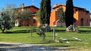 A two-story building with a flat roof and orange walls, surrounded by a well-maintained lawn and tall cypress trees. - Daniele House - Relaxation and Volcanic Water under the Stars Occasum (Canino)