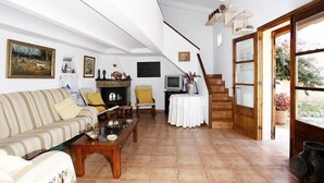 A spacious living room with a sofa, armchairs, a coffee table, and a fireplace. There is a staircase leading to an upper level, and a television on a small table. - Villa with private pool, situated in the heart of the Pollensa countryside (Pollença)