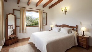 A bedroom with a large bed, wooden headboard, two bedside tables with lamps, a mirror, and a window with curtains. - Villa with private pool, situated in the heart of the Pollensa countryside (Pollença)