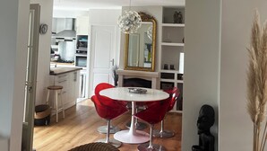 Een moderne keuken met witte kasten, een eethoek met rode stoelen en een rieten bank.