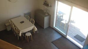 Un coin repas comprenant une table et des chaises, un petit meuble et une porte-fenêtre coulissante donnant sur une terrasse extérieure.