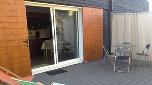 Une terrasse dotée d’une porte-fenêtre coulissante donnant sur une cuisine, de deux chaises pliantes et d’une petite table.