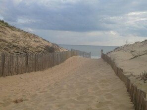 A sandy beach path with a wooden fence on both sides leading to the sea.