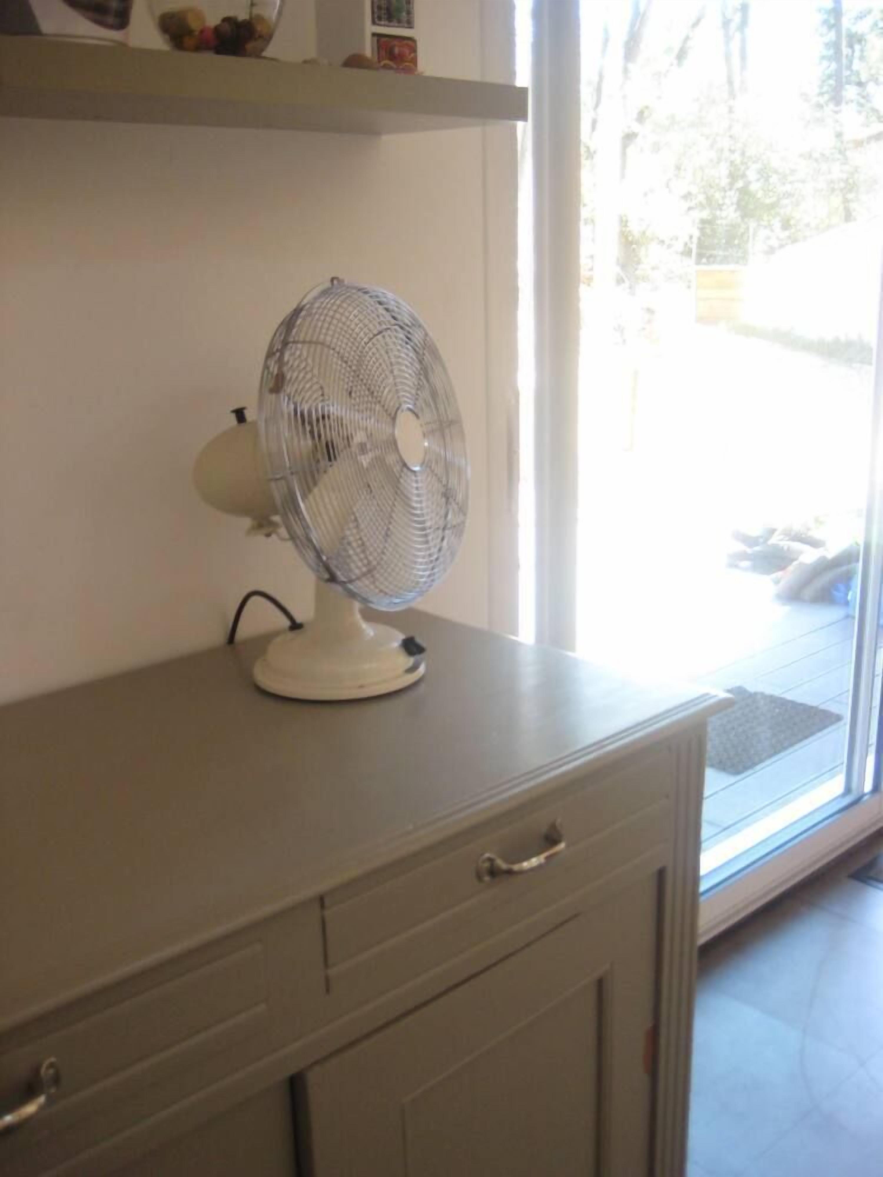 A room with a window, a fan on a dresser, and a door.