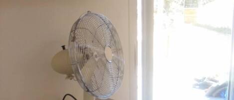 A room with a window, a fan on a dresser, and a door.