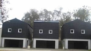 Trois bâtiments noirs identiques, dotés de portes de garage blanches et de petites fenêtres.