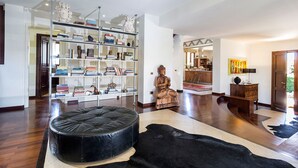 Un salon spacieux avec une grande bibliothèque, un pouf en cuir et une statue.