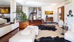 Un salon moderne avec un escalier, un ensemble de canapés, une table basse et un tapis en peau de vache.