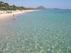 Una playa con agua cristalina, una orilla de arena y montañas al fondo.