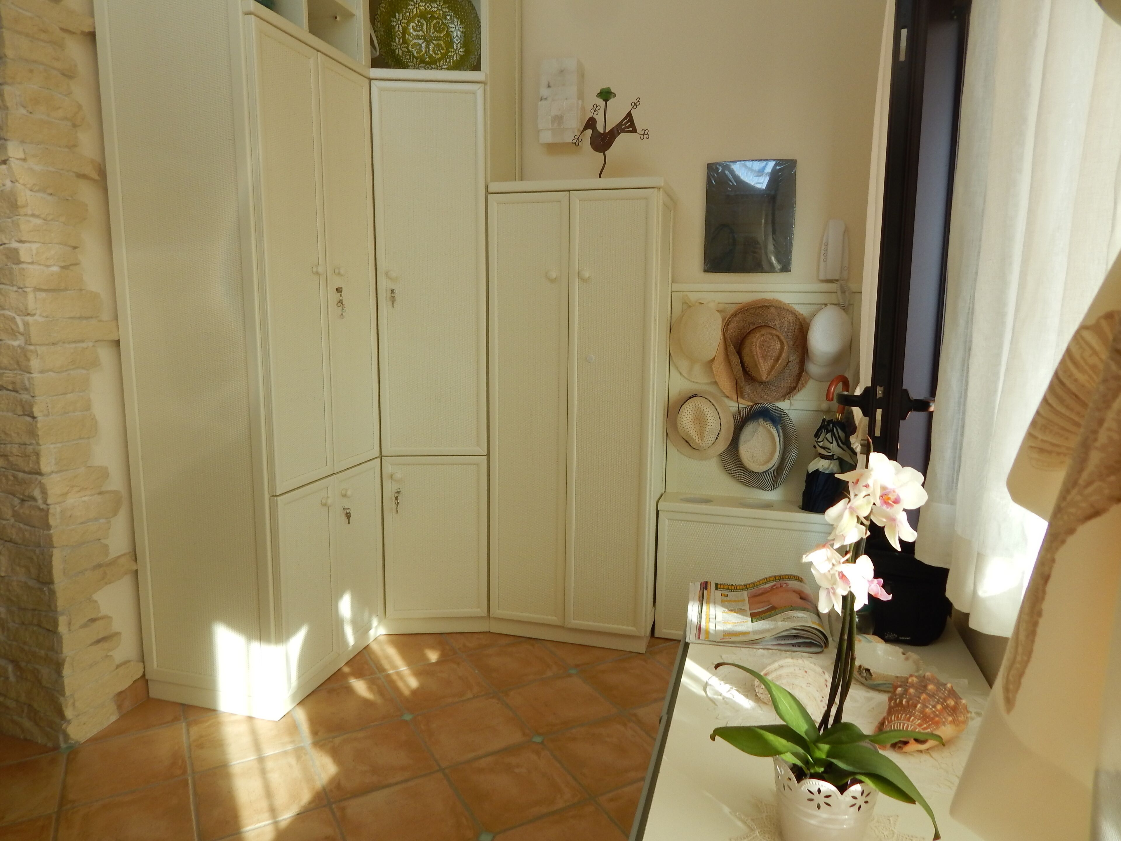 A corner room with a stone wall, a tiled floor, and a white cabinet with hats and a magazine.