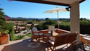 Un patio con mobili in vimini, un tavolo e un ombrellone. Offre una vista panoramica su un paesaggio con montagne e un lago.